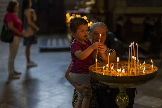 a grandmother helps her grandchild light candles in a church in Lviv