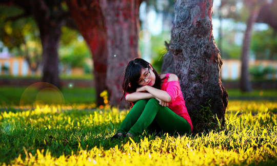 a young woman sitting and resting against a tree