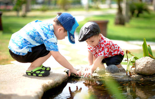 two young boys playing on the edge of a pond