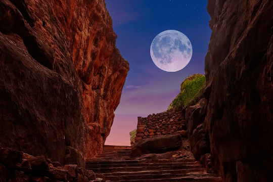 a full moon surrounded by red rock