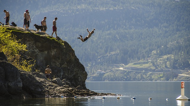 a boy jumping off a cliff with others watching