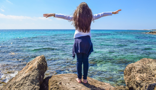 young girl with arms wide open in front of the ocean