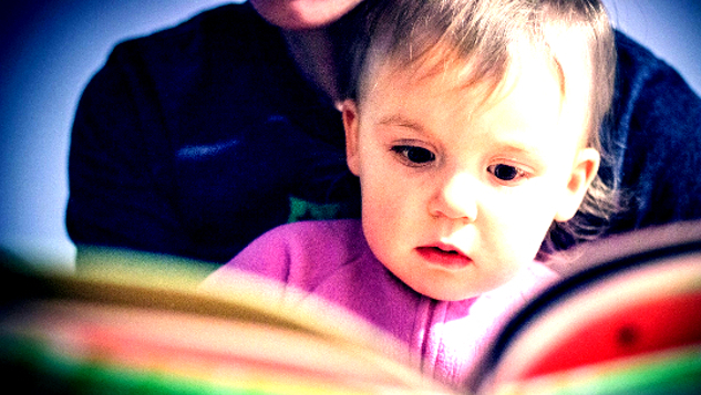 young child on the lap of an adult looking at the pages of a colorful book