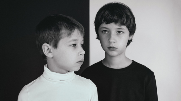 two young boys one dressed in white the other in black in front of a contracting background