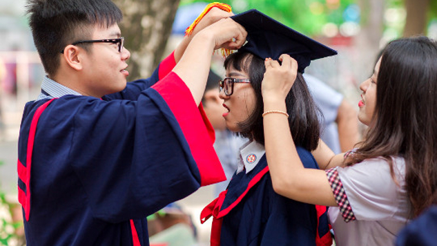 two students adjusting the graduation cap of another
