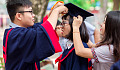 two students adjusting the graduation cap of another